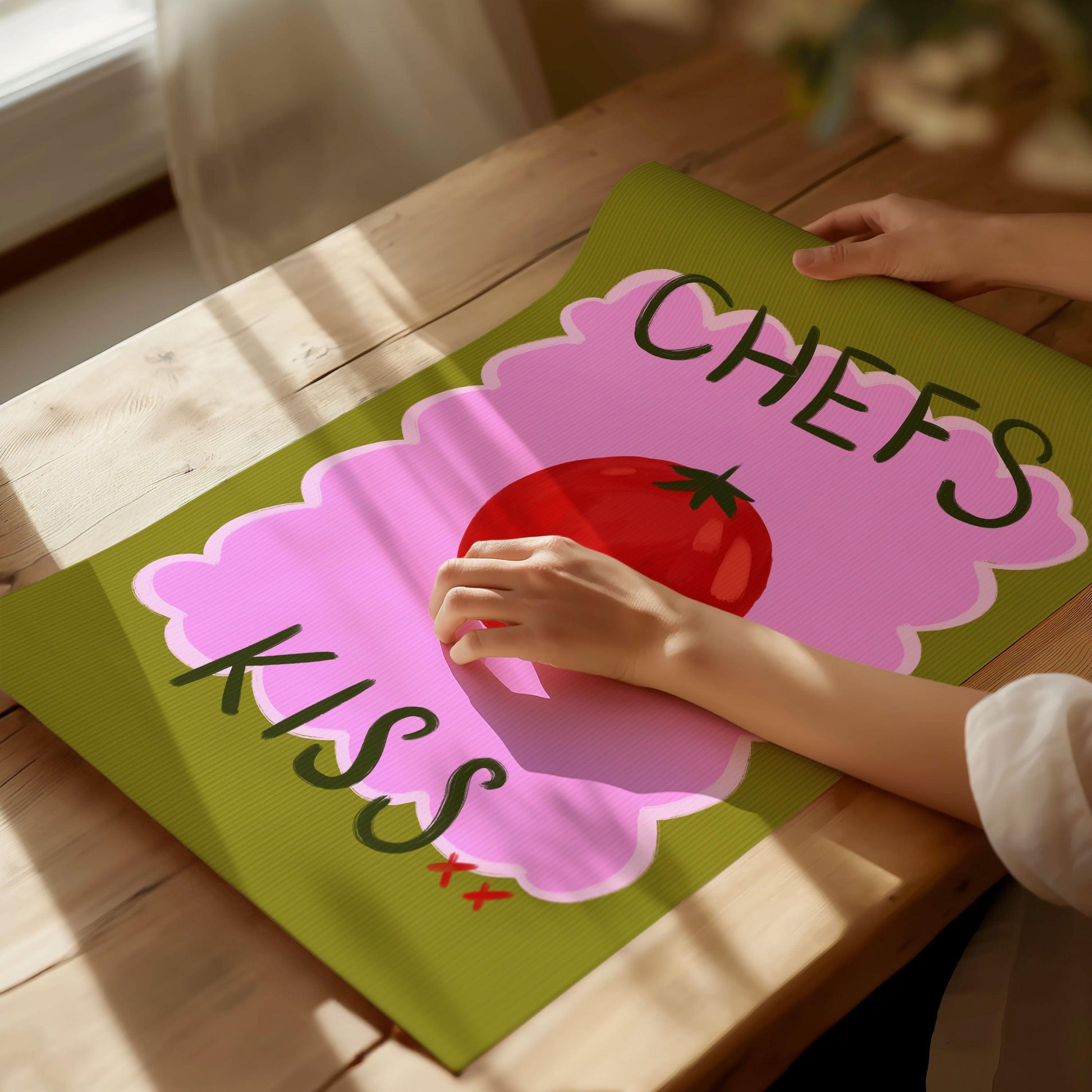 Bright kitchen nook wall art print featuring a painted red tomato with "chefs kiss" handwritten. On a green and pink textured background.