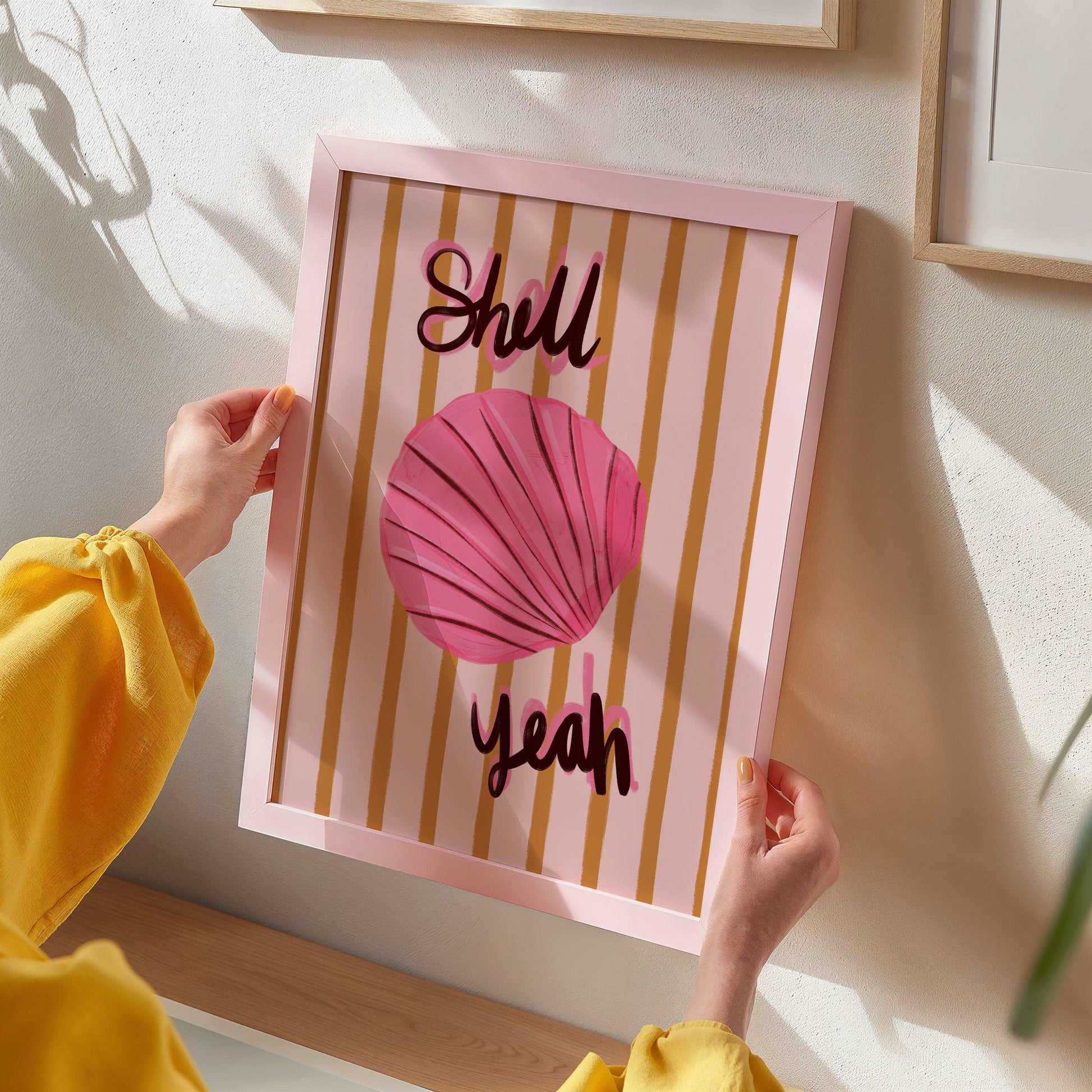 Painterly pink seashell art print with bold handwritten text "Shell Yeah". On a mustard yellow and pink striped background